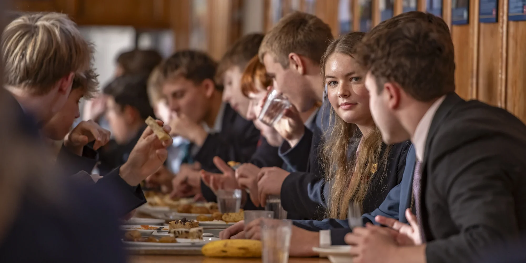 A group of Barnard Castle School students enjoying a meal together at a table in a lively atmosphere.
