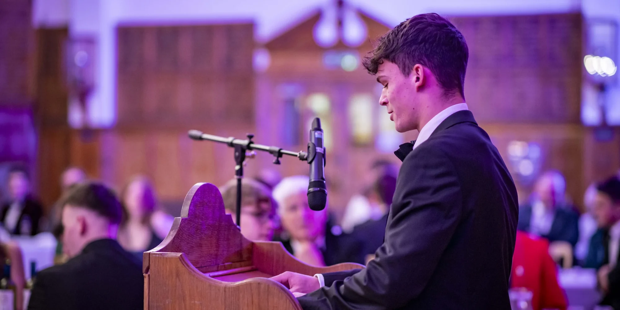 Student speaking in front of school in dining hall.