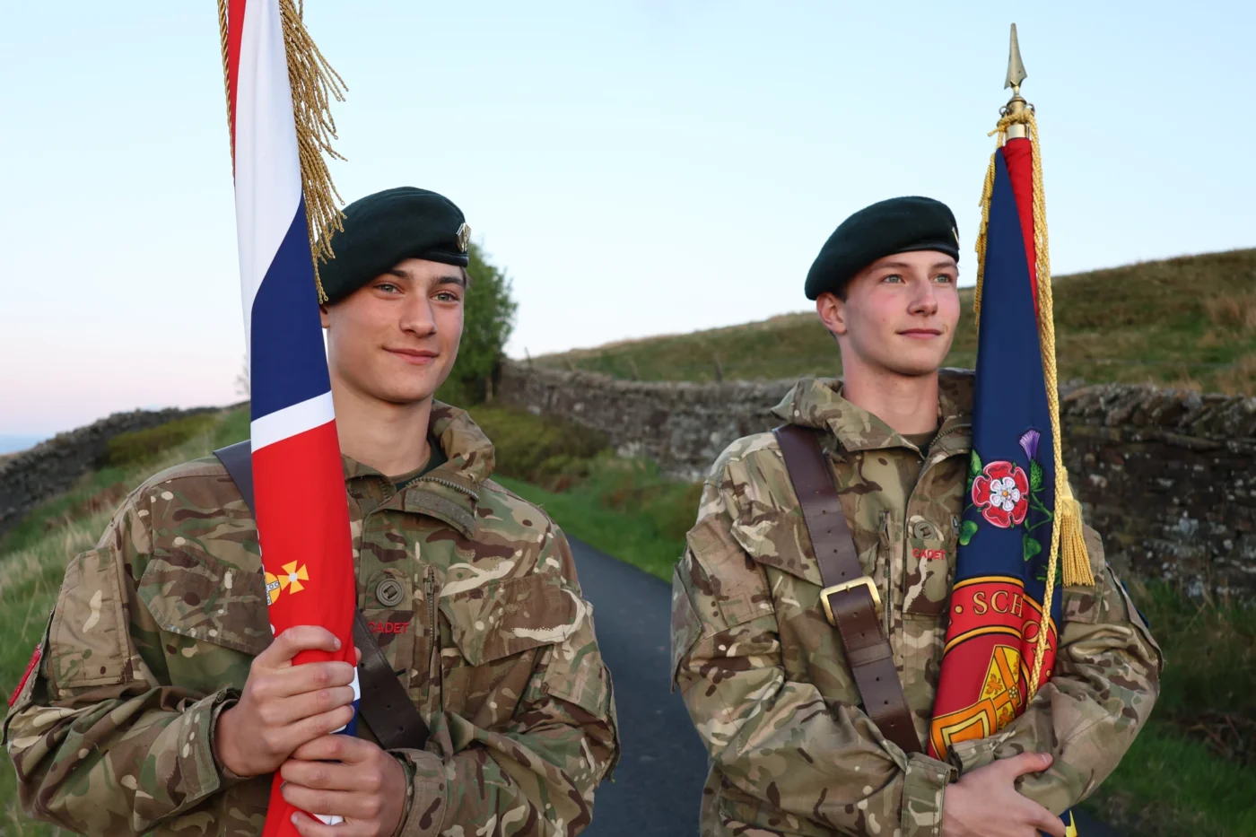 Two cadets in uniform on country lane holding flags.