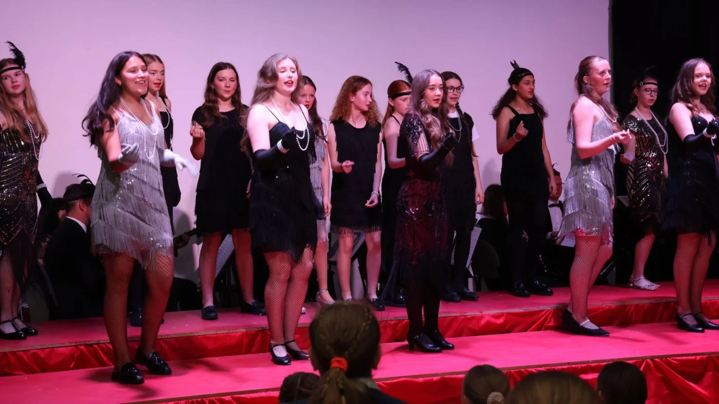 Students in 1920s-style dresses singing on stage.