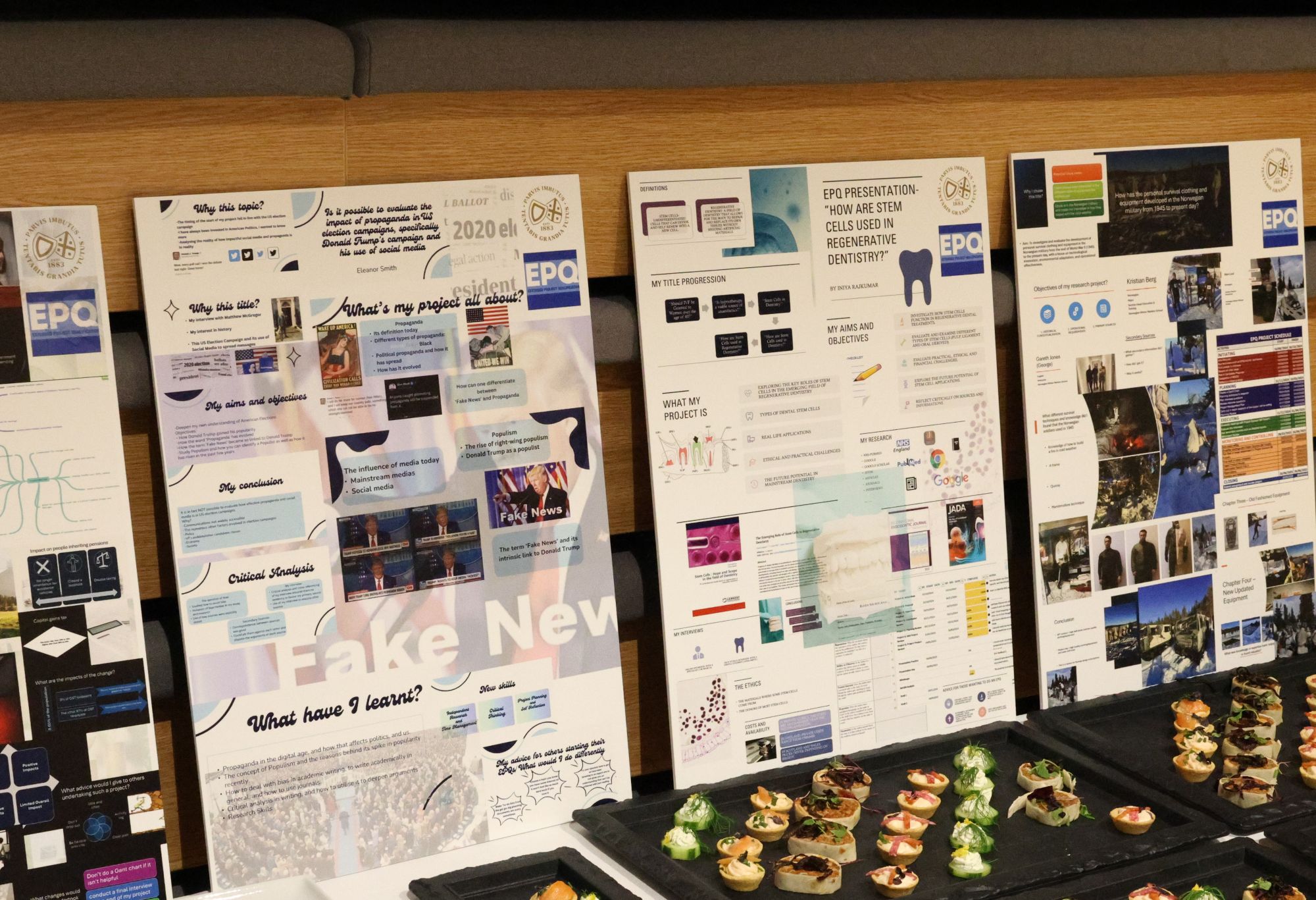 A row of colourful EPQ research posters displayed above trays of bite-sized appetisers at an event